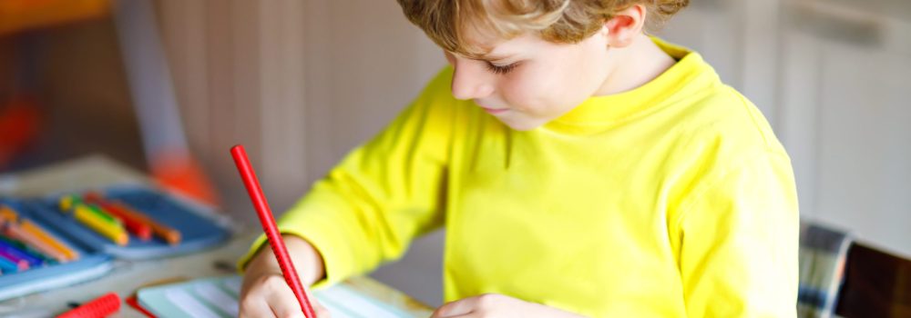 Happy smiling little kid boy at home making homework at the morning before the school starts. Little child doing excercise, indoors. Elementary school and education: Boy writing letters and numbers.