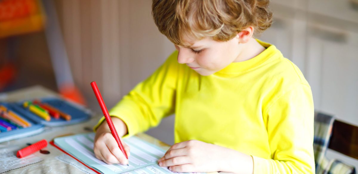 Happy smiling little kid boy at home making homework at the morning before the school starts. Little child doing excercise, indoors. Elementary school and education: Boy writing letters and numbers.