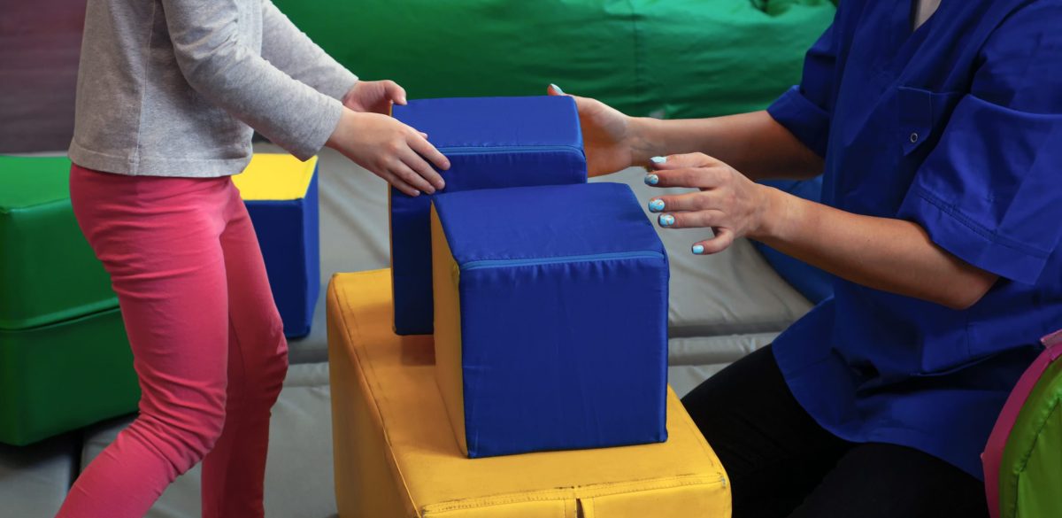 girl with a psychologist plays in multi-colored soft cubes. preschool education