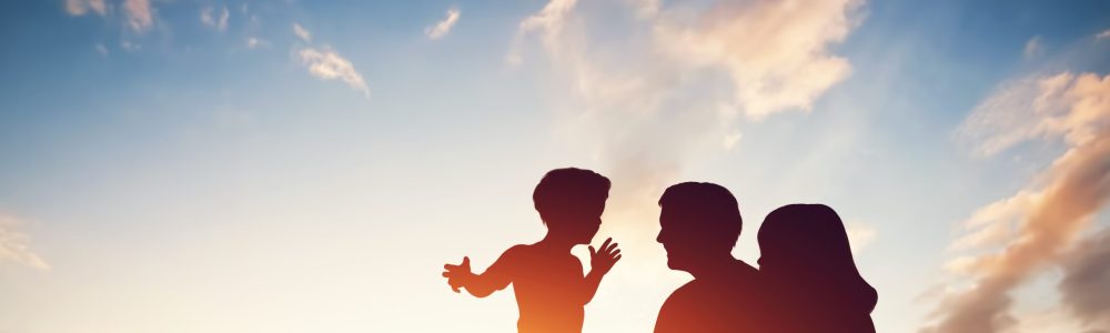 Happy family together, parents with their little child sitting on grass at sunset