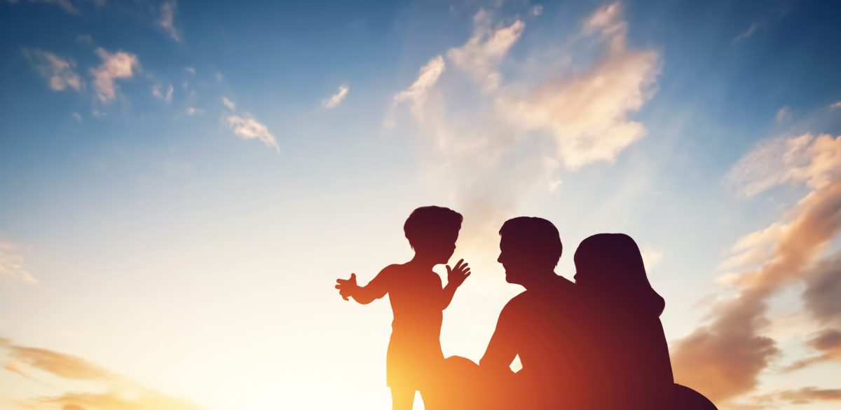 Happy family together, parents with their little child sitting on grass at sunset